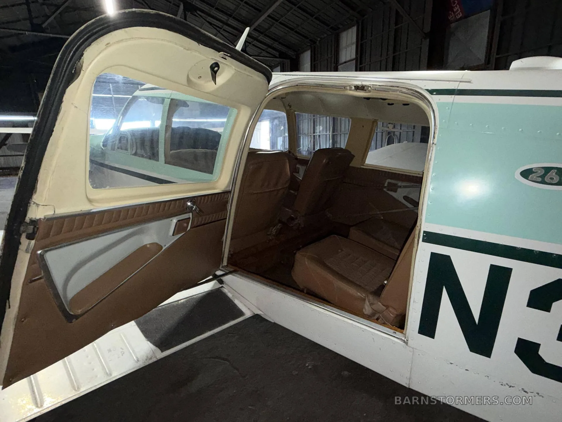 The interior cabin of a light aircraft, showing brown seats and the open entry door.