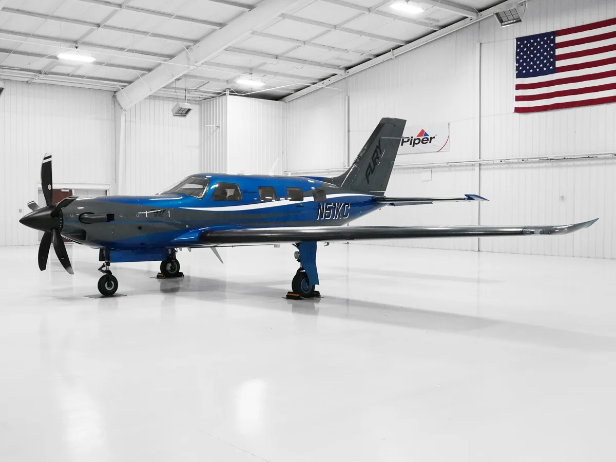A blue and grey Piper M700 Fury turboprop aircraft with registration N51KC is parked inside a brightly lit white hangar.