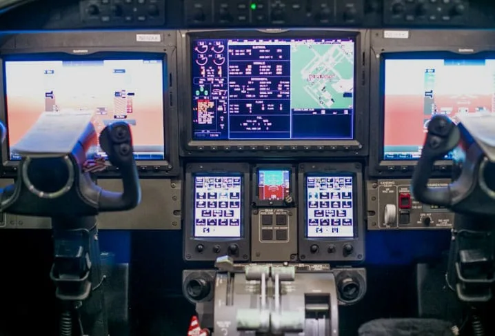 The modern cockpit of an aircraft with multiple digital flight displays, yokes, and throttle quadrant.