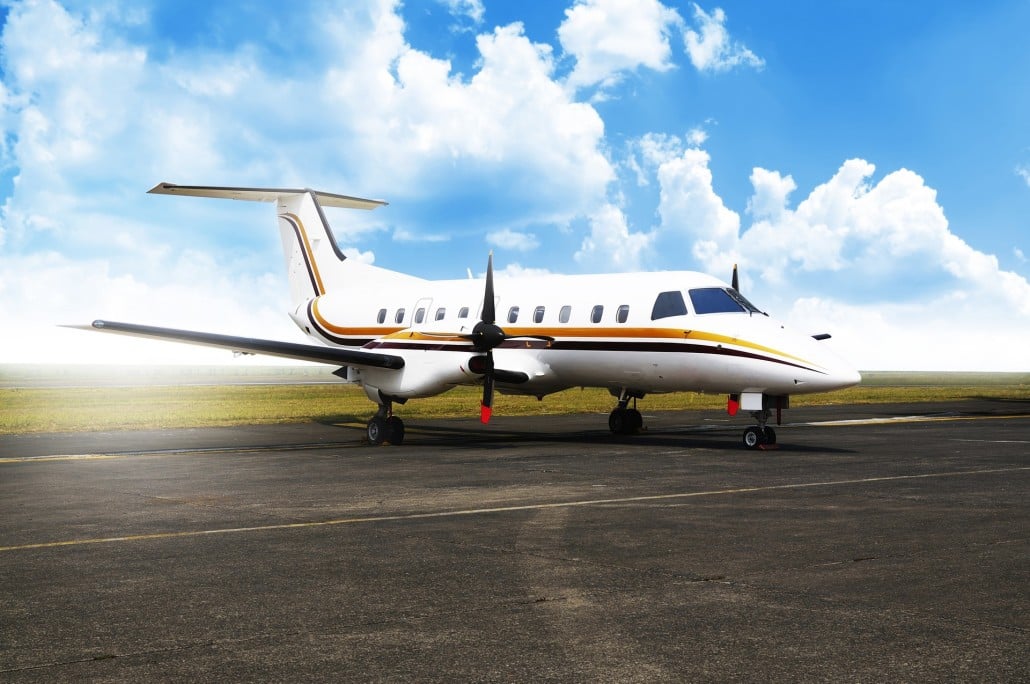 A white turboprop aircraft with gold and black stripes parked on an asphalt runway under a partly cloudy sky.