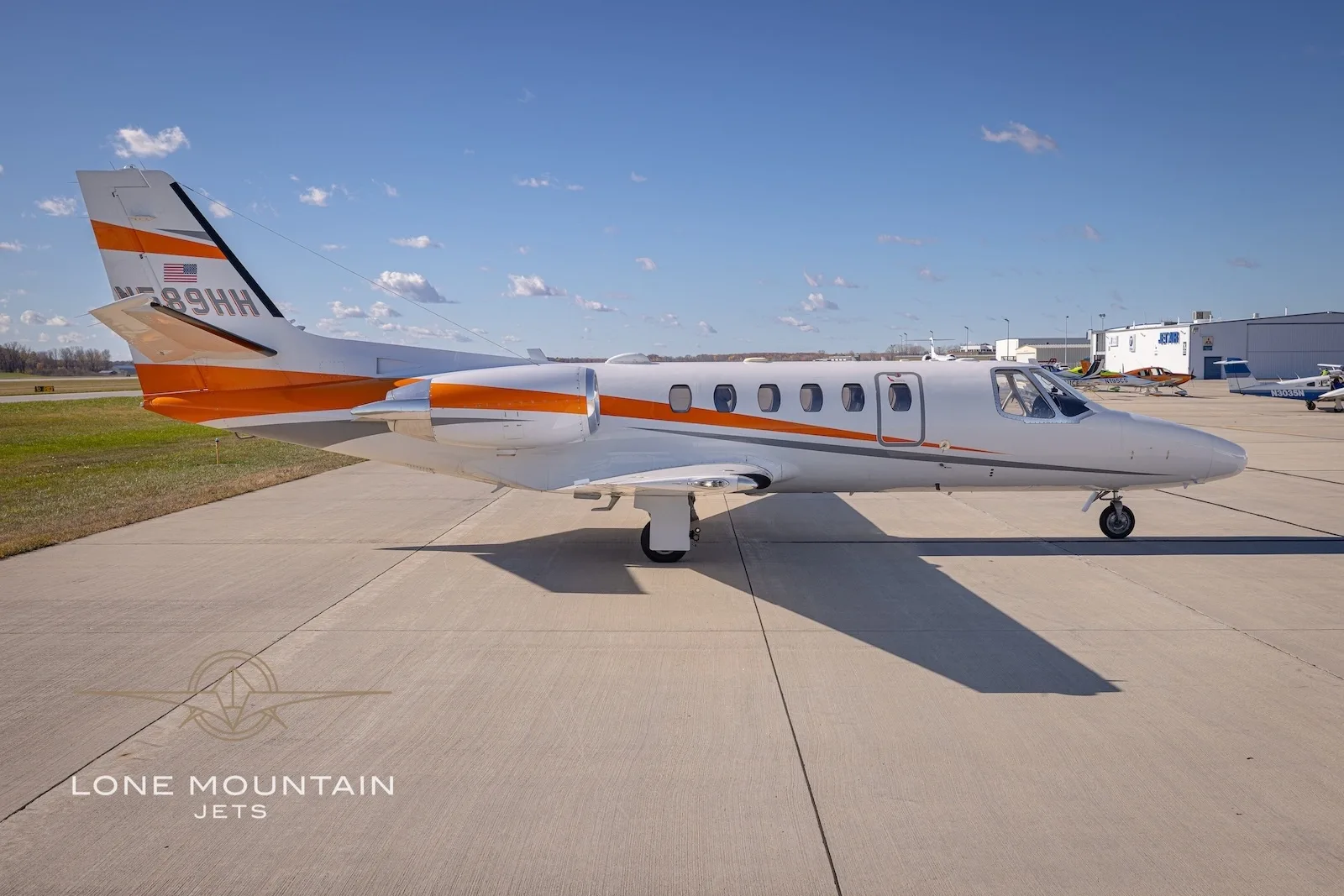 A side view of the white Cessna Citation Bravo business jet N589HH with orange and grey stripes on the tarmac.