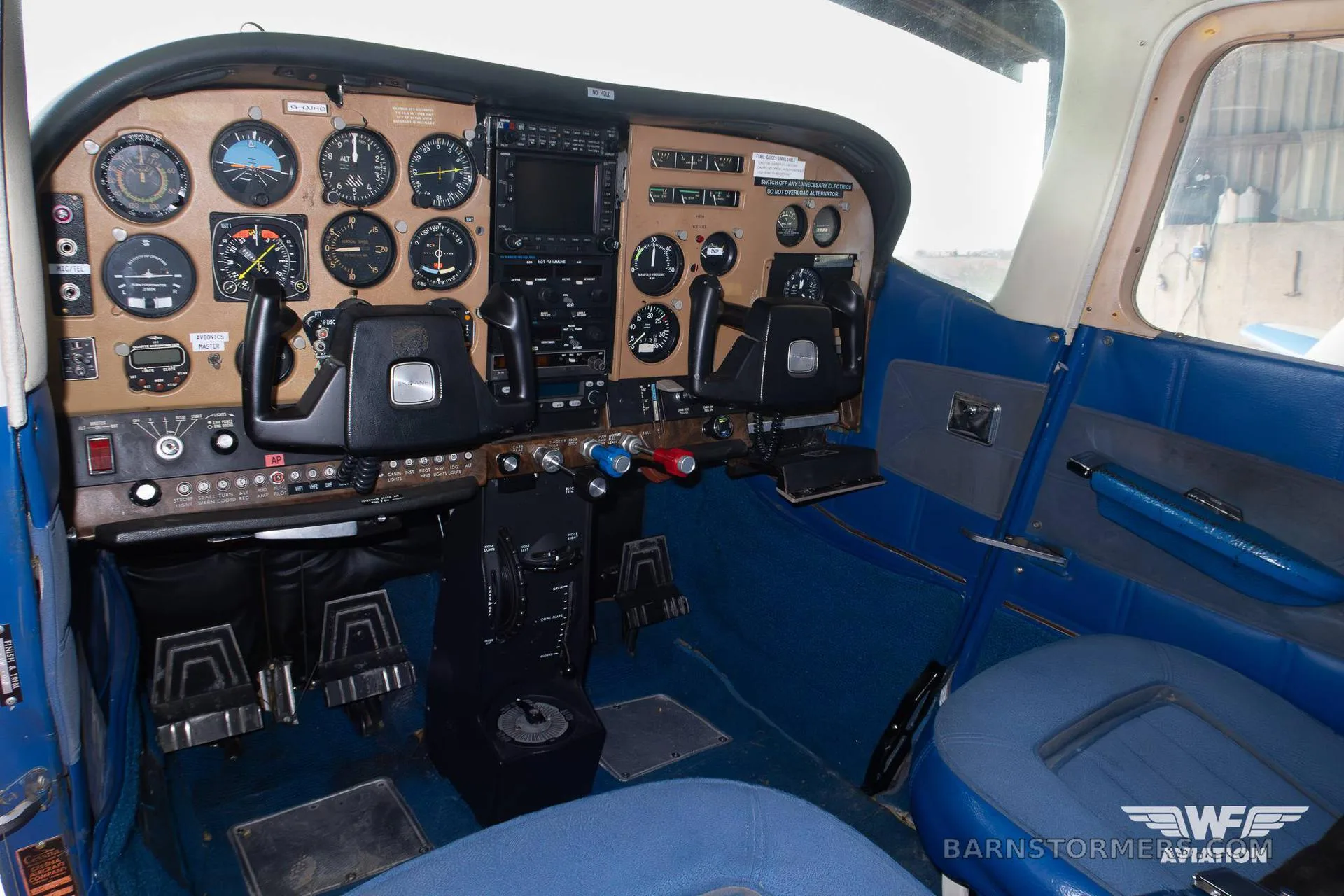 The cockpit of a Cessna aircraft with a brown instrument panel, dual yokes, and blue seats.
