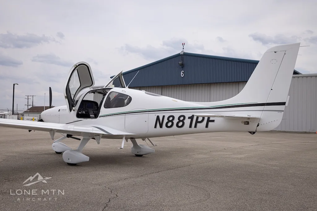 A rear-side view of a white Cirrus SR22 aircraft with N881PF registration and open doors, parked on an asphalt ramp.