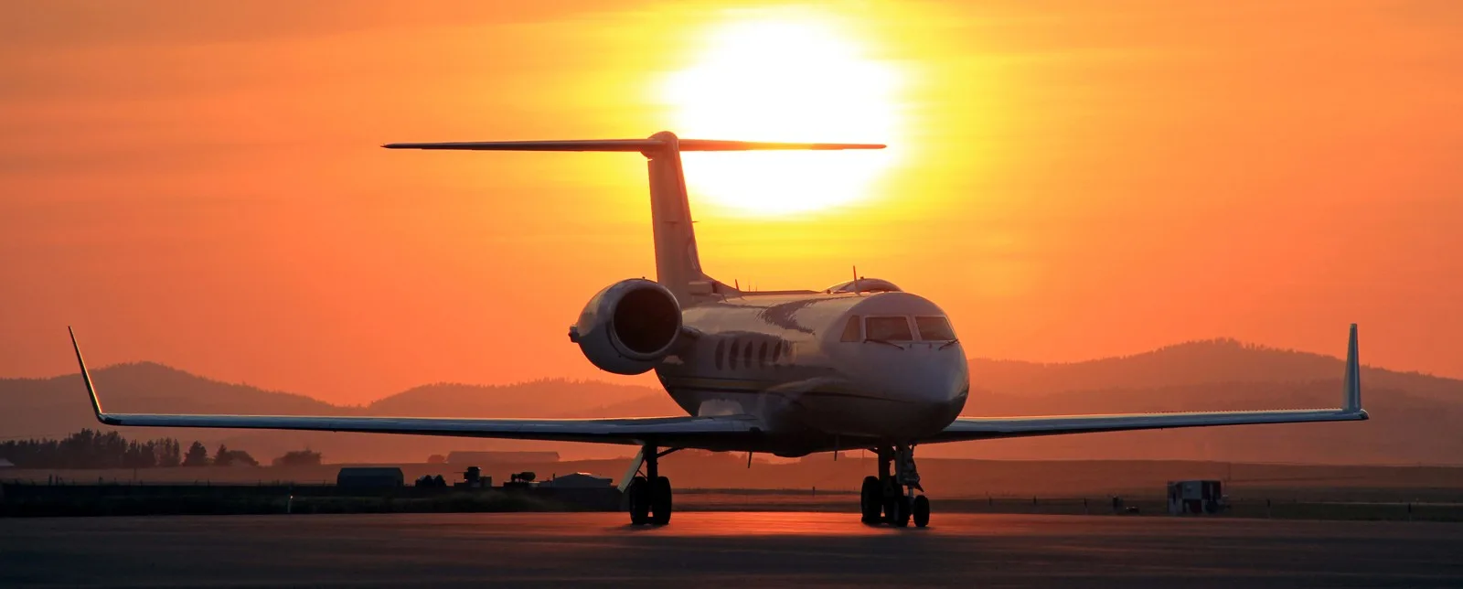 A white business jet, possibly a Gulfstream, on a tarmac silhouetted against a vibrant orange sunset.