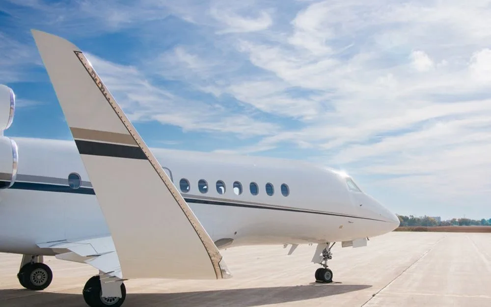 A close-up side view of the front fuselage and tail of a white Dassault Falcon 900EX business jet on an airfield.