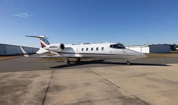 A white Learjet 60 with red and black accents on the tail, registration N30GJ, parked on a tarmac under a clear blue sky.