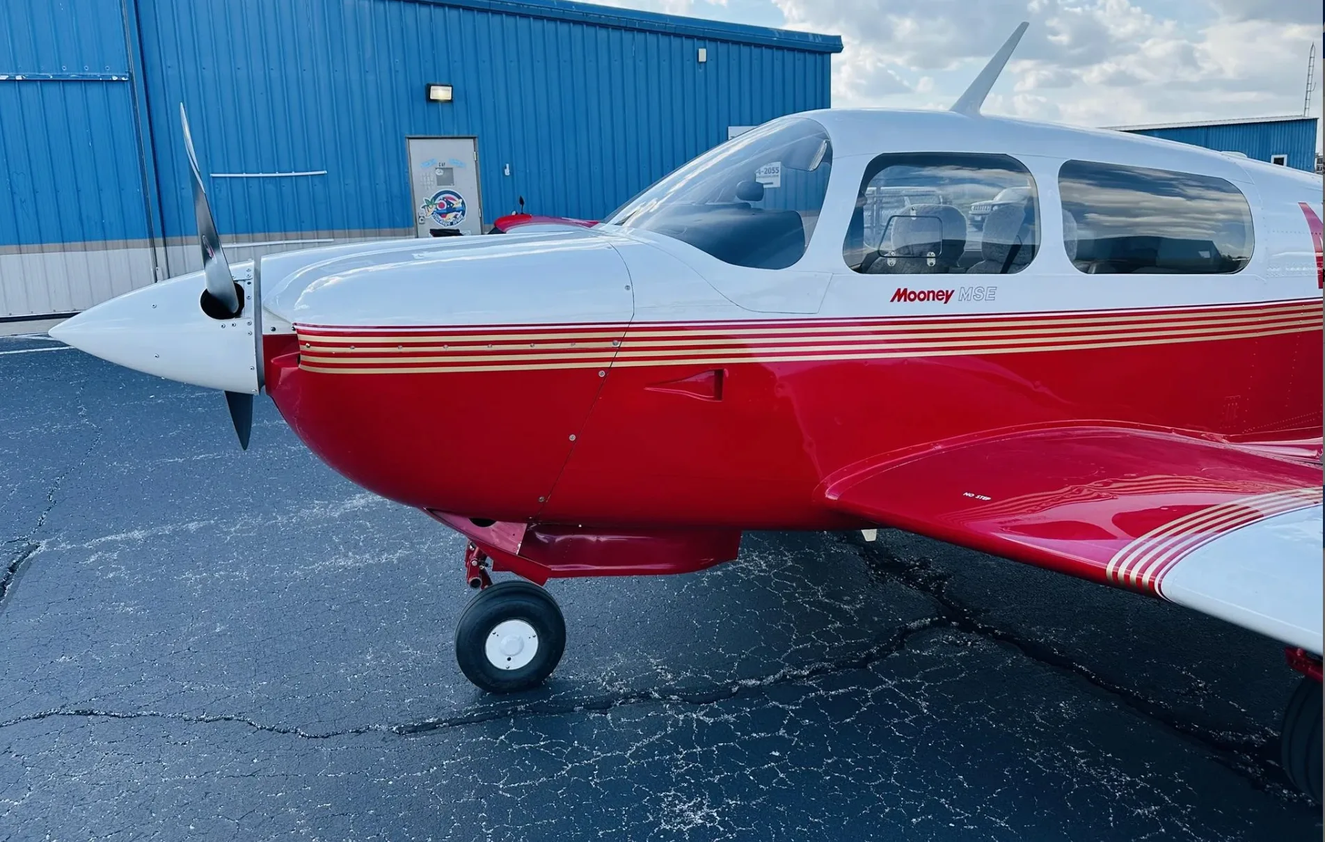 A close-up of the front right side of a red and white Mooney M20J aircraft on a tarmac.