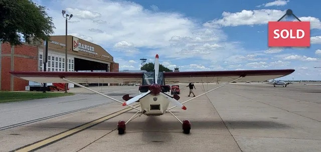 Front view of a light aircraft on the tarmac with a red and white paint scheme.