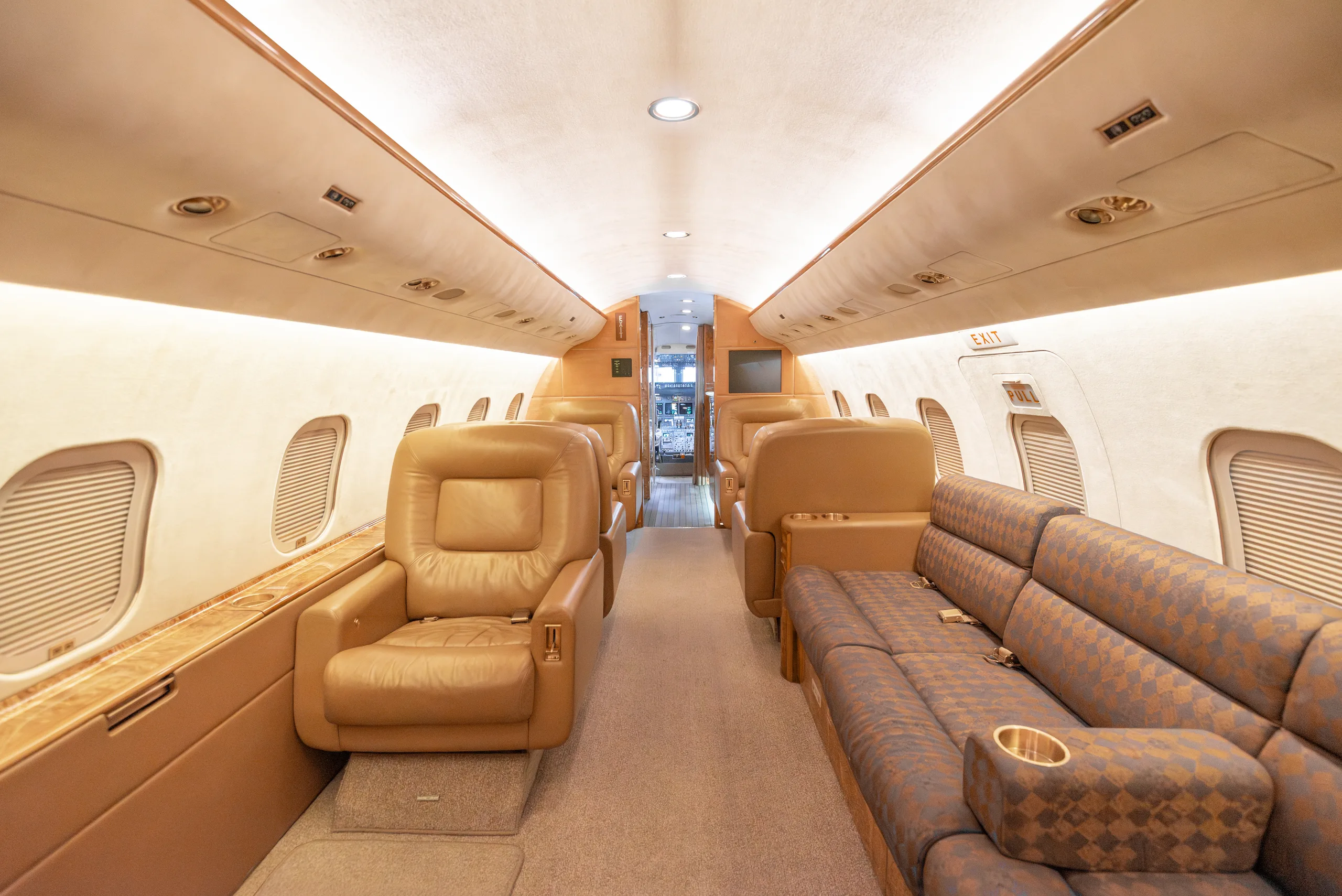 The luxurious interior of a private jet cabin with tan leather seats and a patterned sofa.