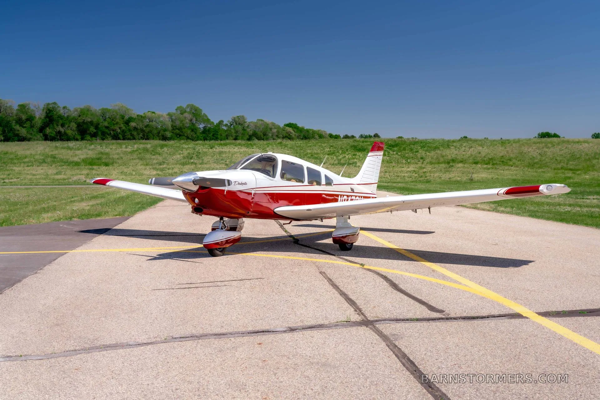 A red and white Piper Dakota aircraft is parked on an asphalt runway under a clear blue sky.