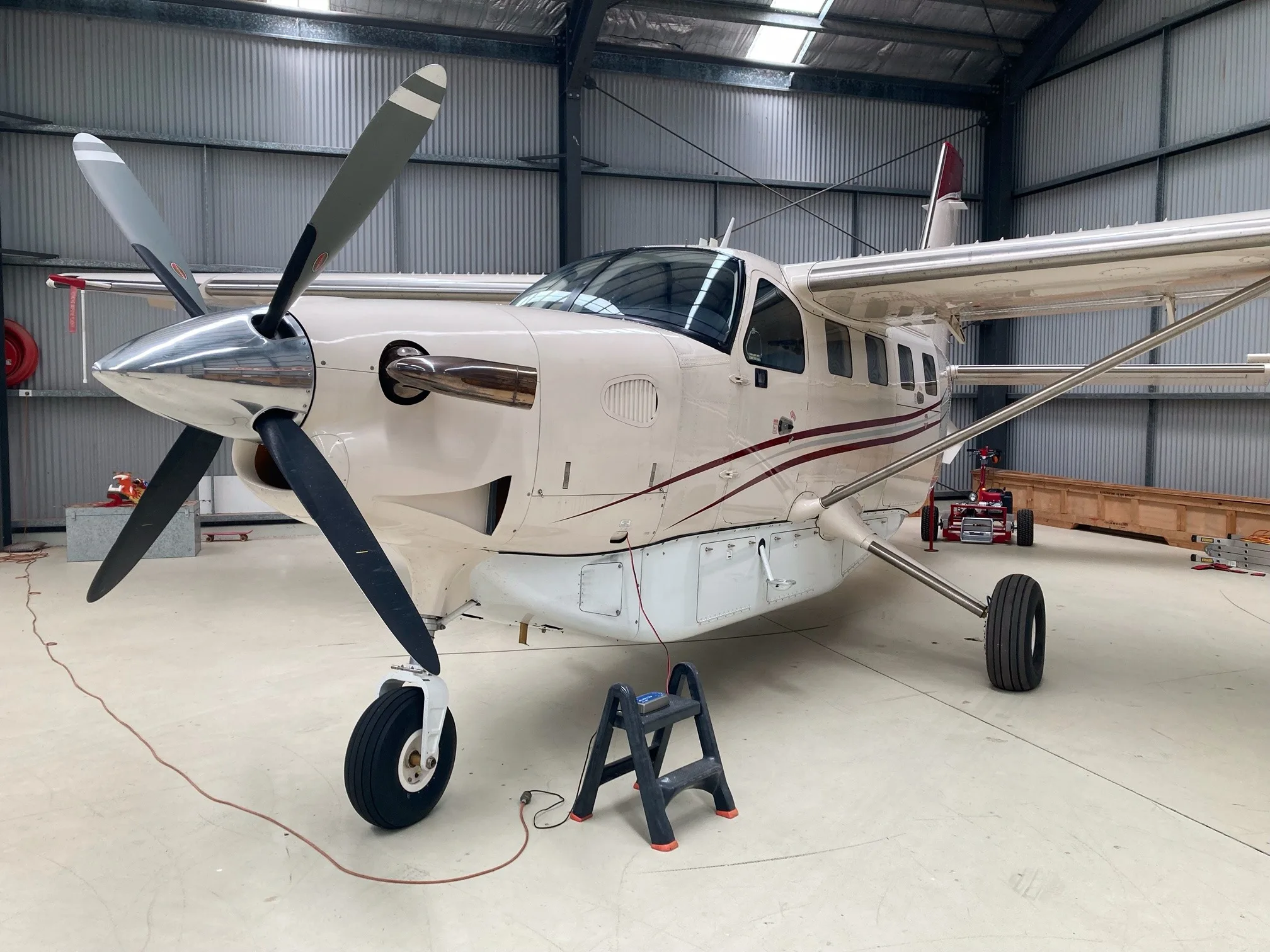 A beige Quest Kodiak 100 aircraft with red stripes, parked inside a hangar with its propeller visible.