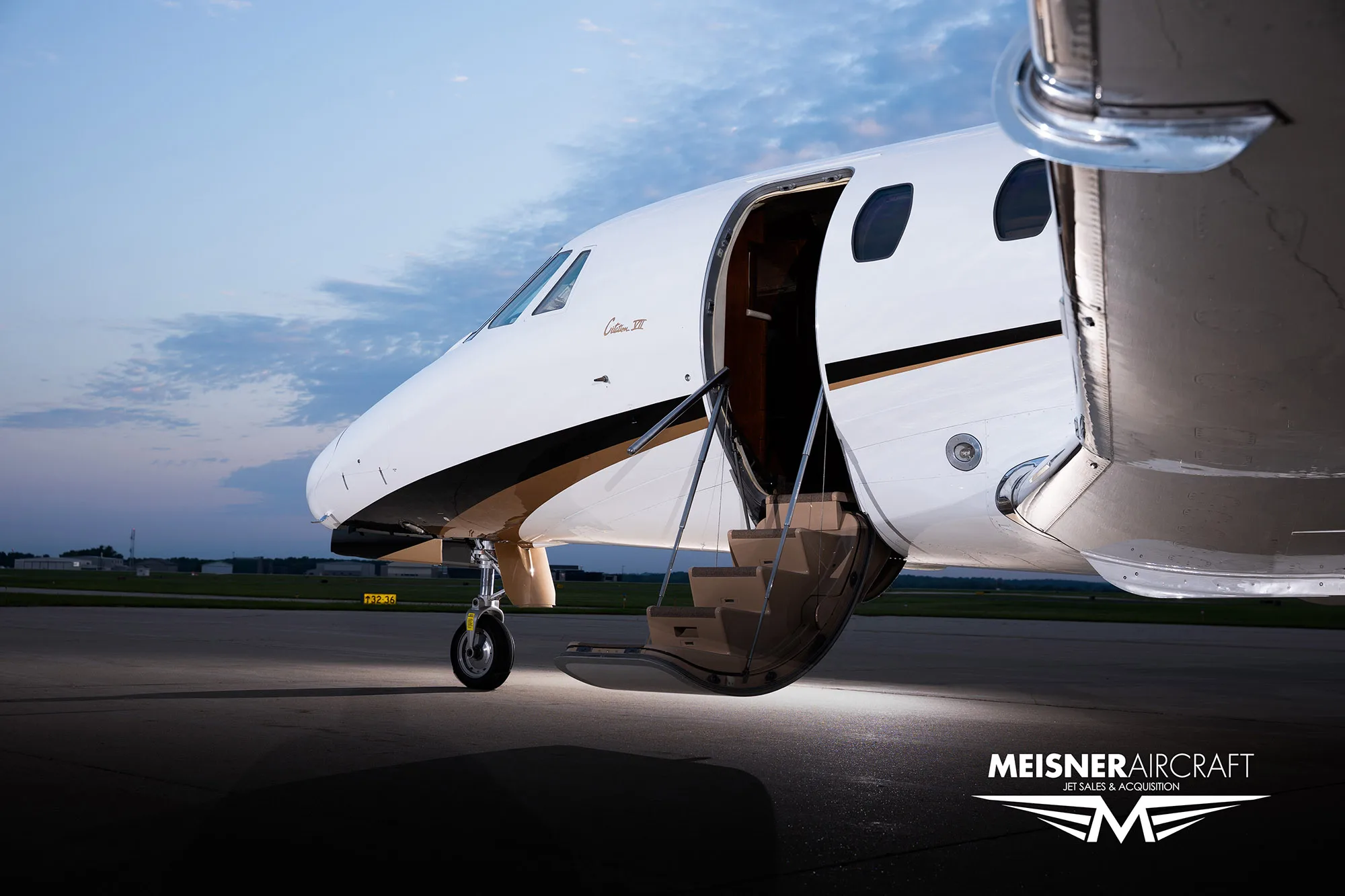A close-up view of the front of a white Cessna Citation business jet with its main entry door open and stairs extended on a tarmac at dusk.