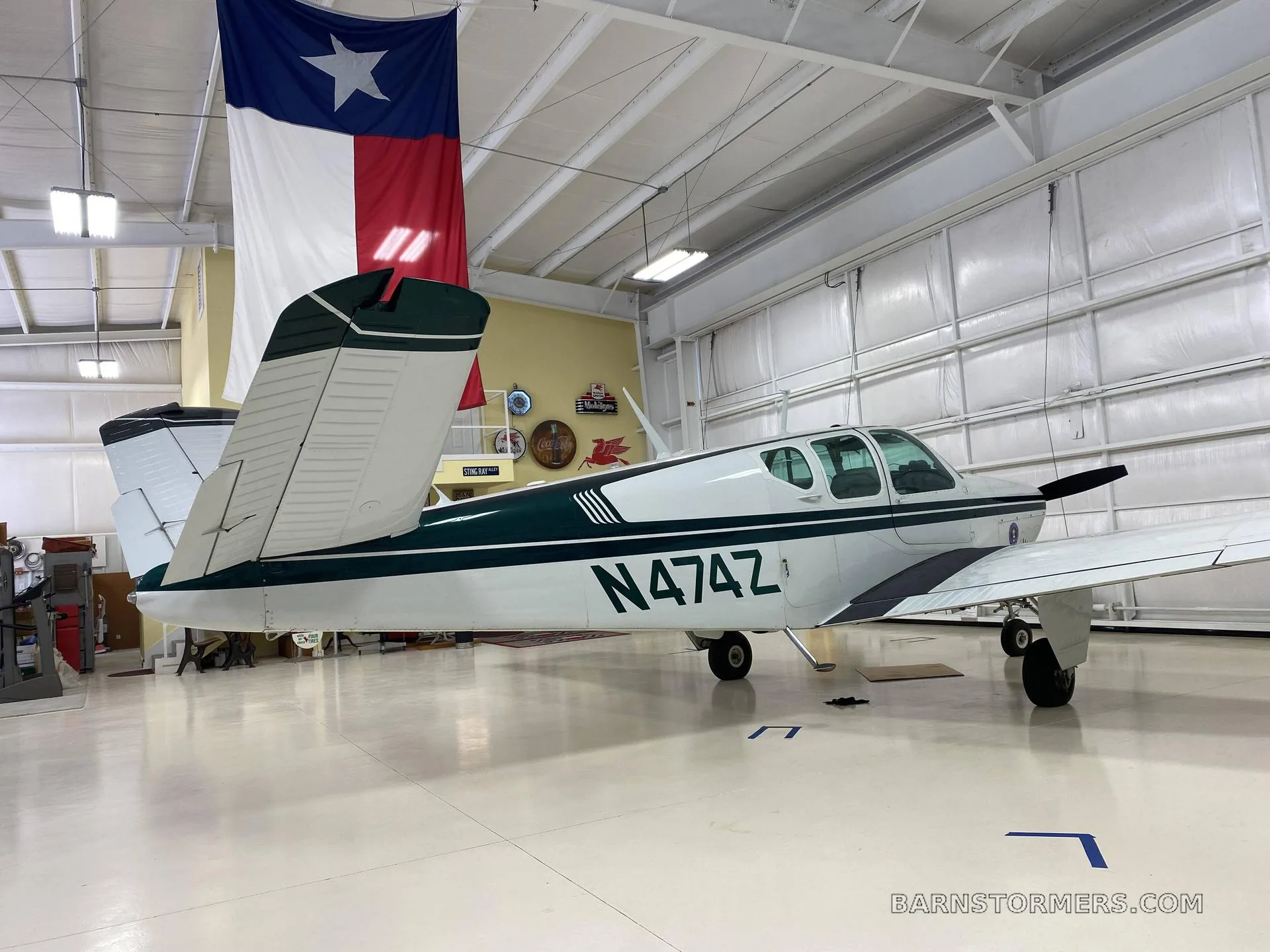 A white and dark green Beechcraft Bonanza with registration N474Z is parked in a hangar, viewed from the rear-left.
