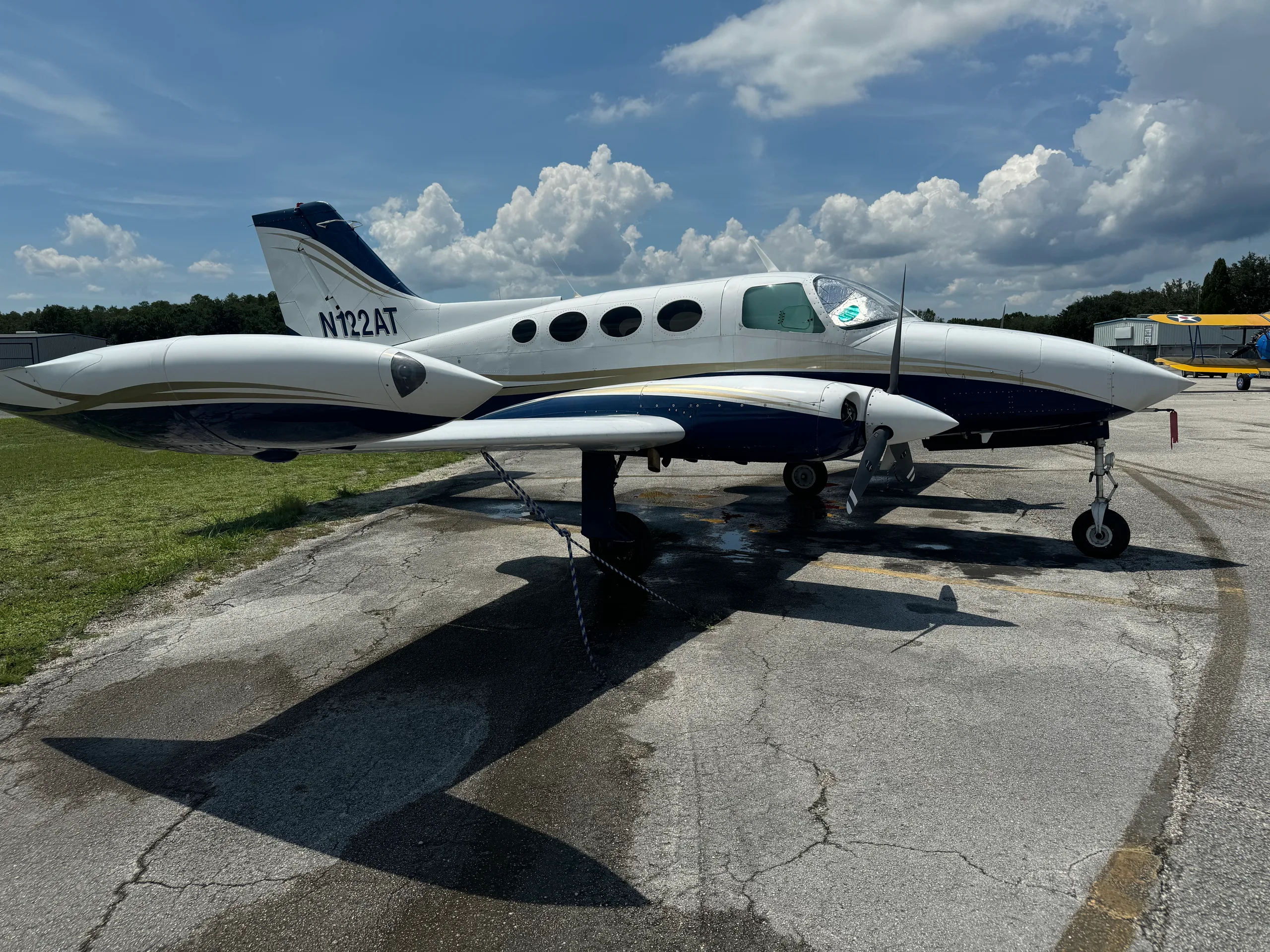 A white and blue Cessna 401 (or similar twin-engine prop) aircraft, registration N122AT, parked on an asphalt ramp under a partly cloudy sky.