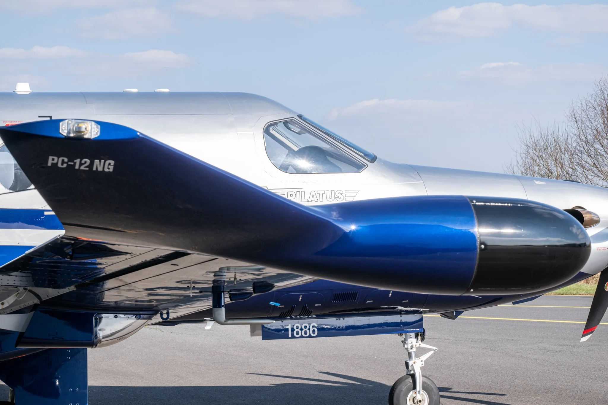 A close-up side view of the silver and blue Pilatus PC-12 NG aircraft's fuselage and propeller.