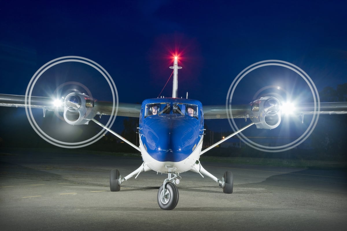 Front view of a blue and white aircraft with spinning propellers at night.