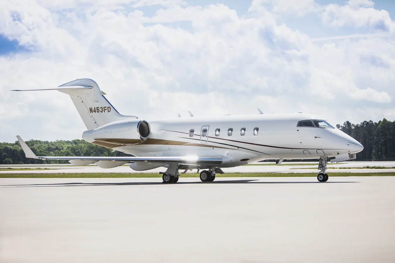 Side profile of a white business jet with N453FD registration, showing gold and maroon accent stripes, on an airfield.