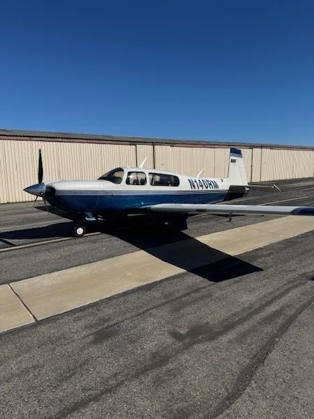 A white and blue single-engine propeller aircraft, N14DRM, parked on an asphalt tarmac in front of a hangar under a clear blue sky.