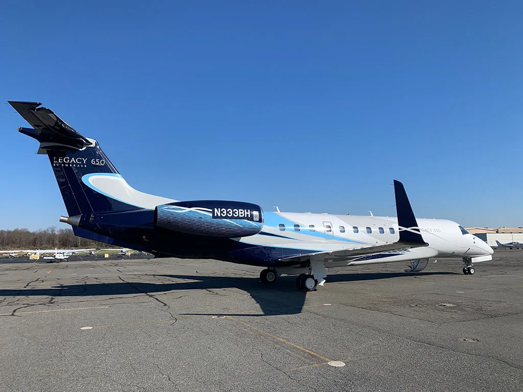 A side view of the Embraer Legacy 650 (N333BH) with its distinctive blue and white livery on an airport tarmac.