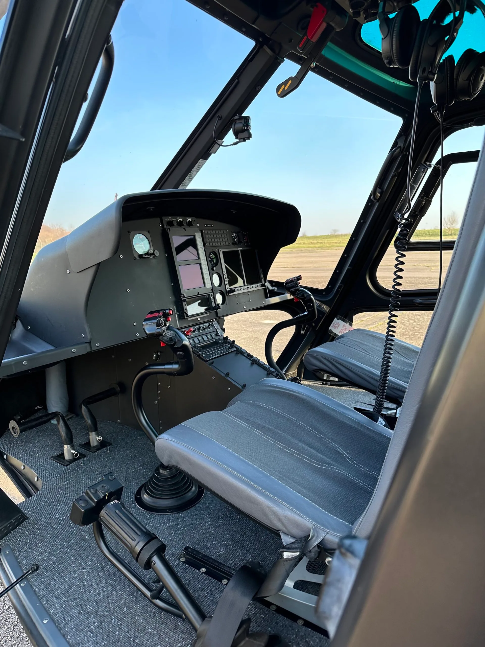 Helicopter cockpit with modern avionics and controls, seen from the passenger seat.