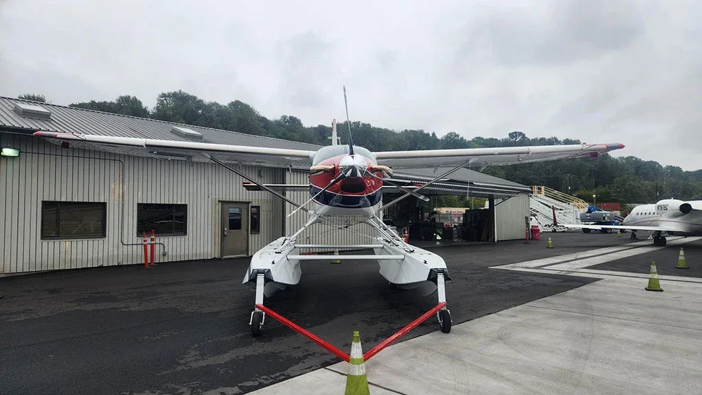 A front view of a red, white, and blue Quest Kodiak 100 on amphibious floats parked on an asphalt apron.