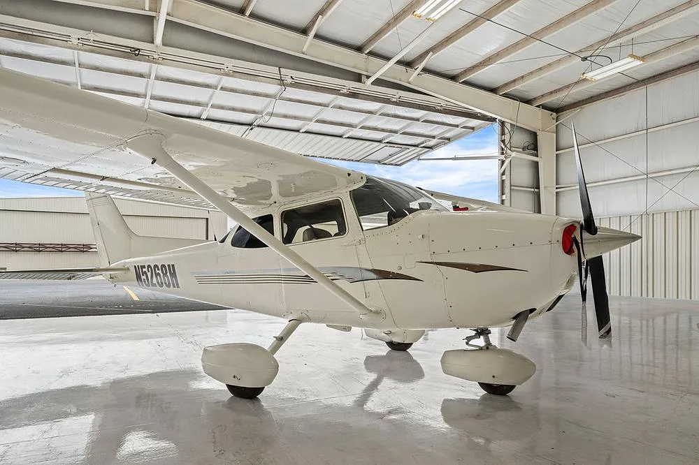 A low-angle side-front view of the white Cessna 172, registration N5268H, in a hangar with an open door.