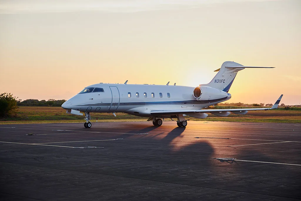 A white Bombardier Challenger 300 private jet with blue stripes, registration N311FC, on an airfield at sunset.