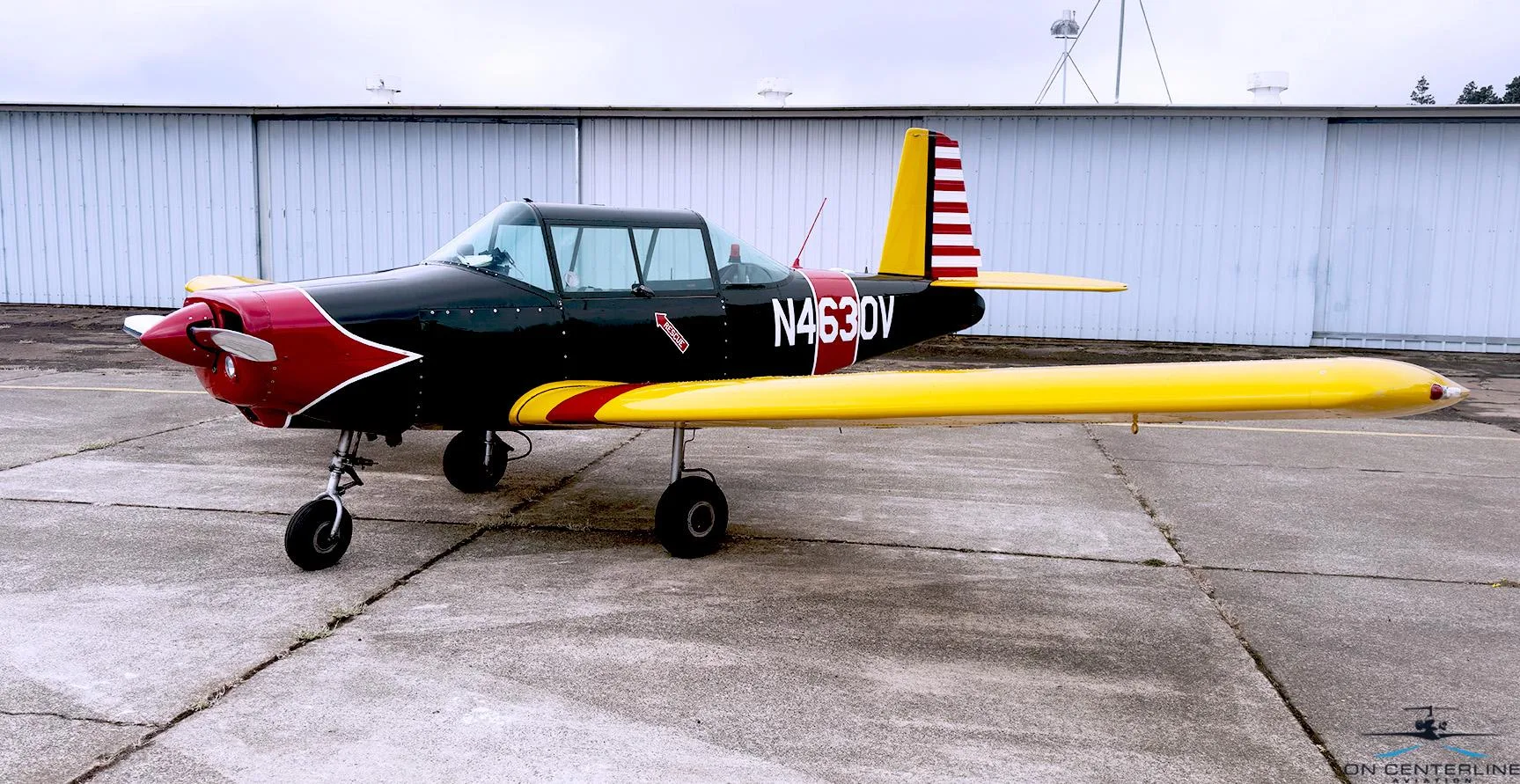 A side view of the N4630V aircraft, featuring its black, red, and yellow paint scheme, parked on an airfield.