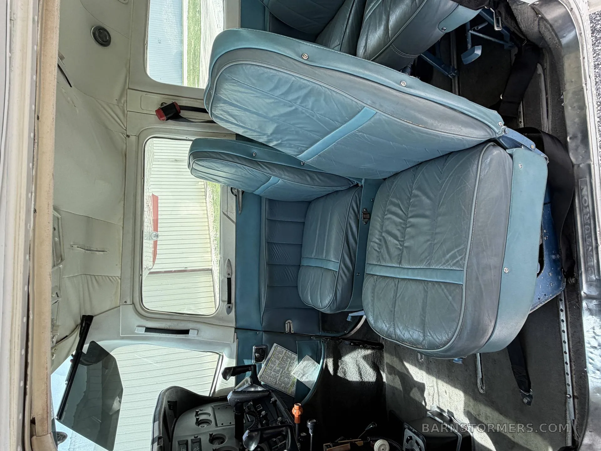 The light blue leather seats of an aircraft cabin are visible, with the cockpit area in the foreground.