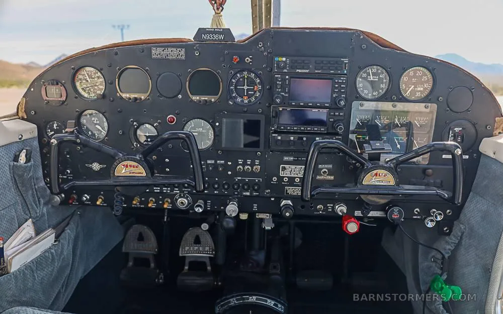 The cockpit instrument panel of a Piper Cherokee 235B with dual yokes and various gauges and screens.