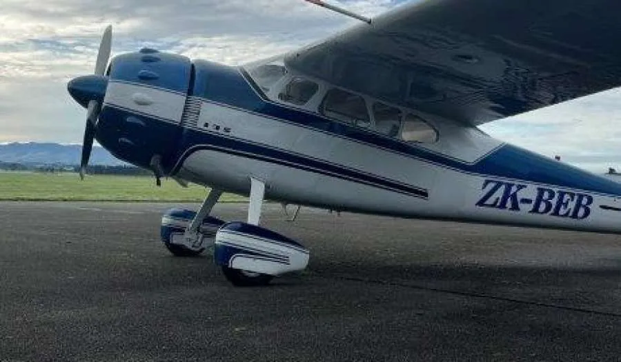 A blue and white single-engine propeller aircraft with registration ZK-BEB parked on an airfield with mountains in the background.