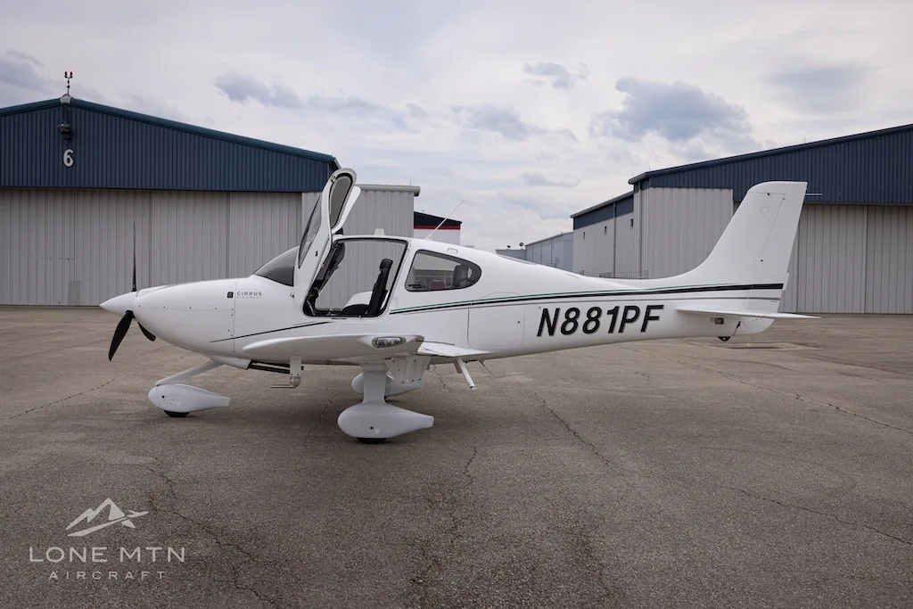 A white Cirrus SR22 aircraft with N881PF registration and green accent stripes, parked on an asphalt ramp with its doors open.
