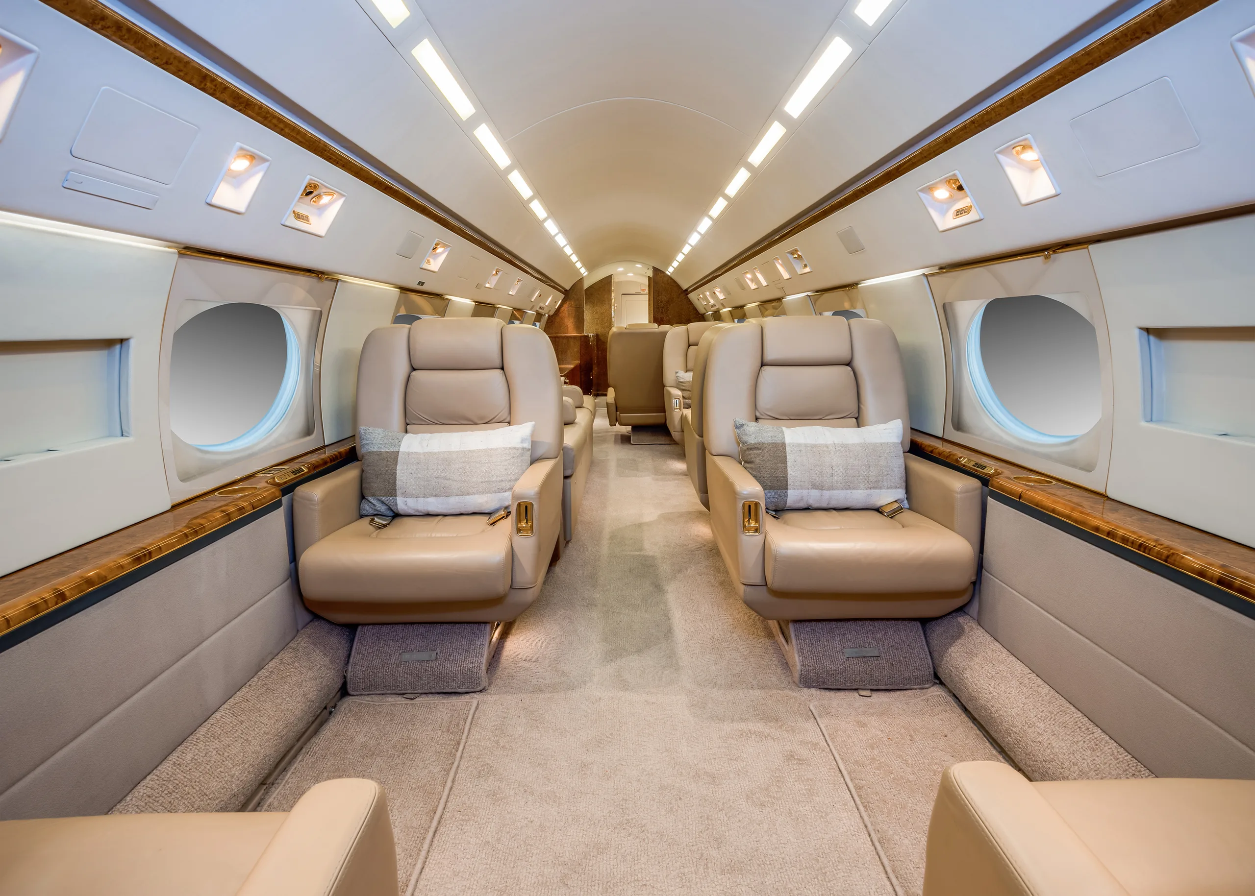 A luxurious aircraft cabin with two rows of beige leather seats facing each other, each with a plaid pillow.