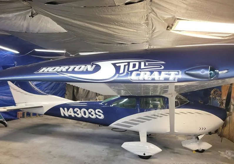 A side view of a blue and white Cessna N4303S in a hangar, with "HORTON STOLCRAFT" visible on the wing.