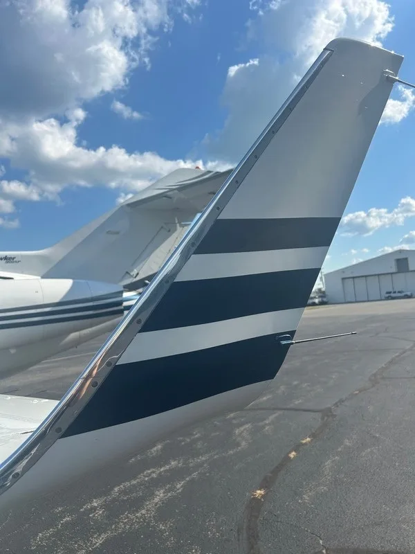 A close-up view of the vertical stabilizer of a white business jet, featuring two dark blue horizontal stripes.