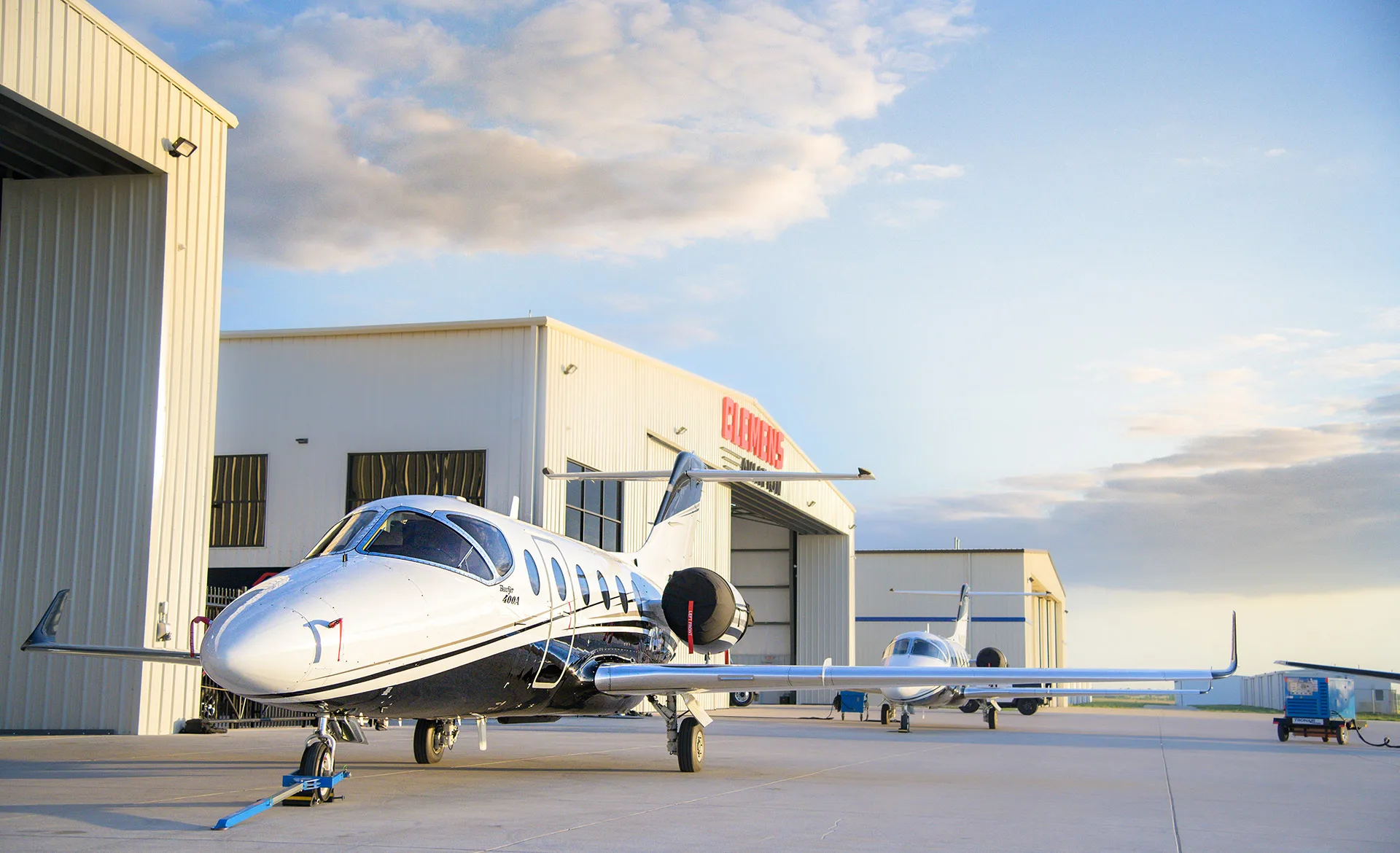 A white and black Beechjet 400A business jet is parked on an airfield in front of hangars under a cloudy sky.