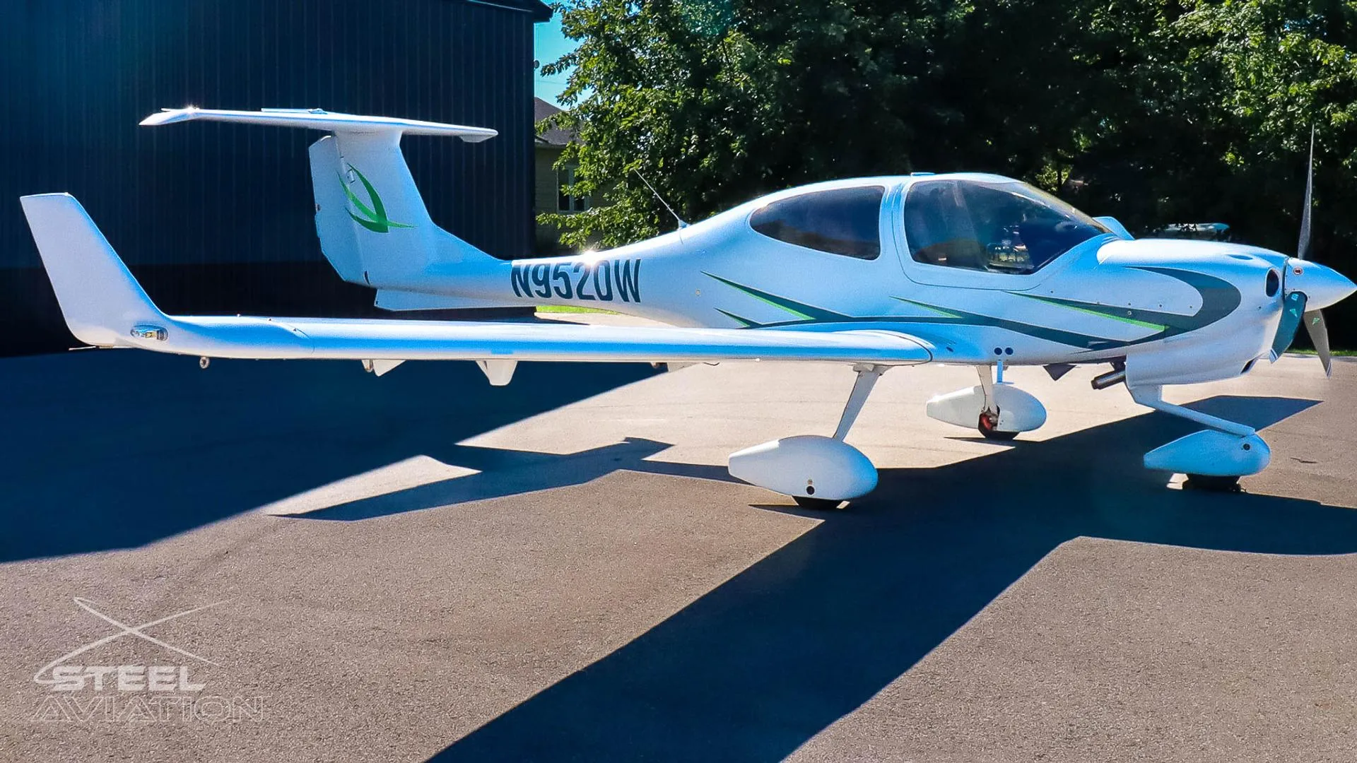 Side view of a white Diamond DA40 aircraft with green accents and registration N952DW parked on an asphalt surface.