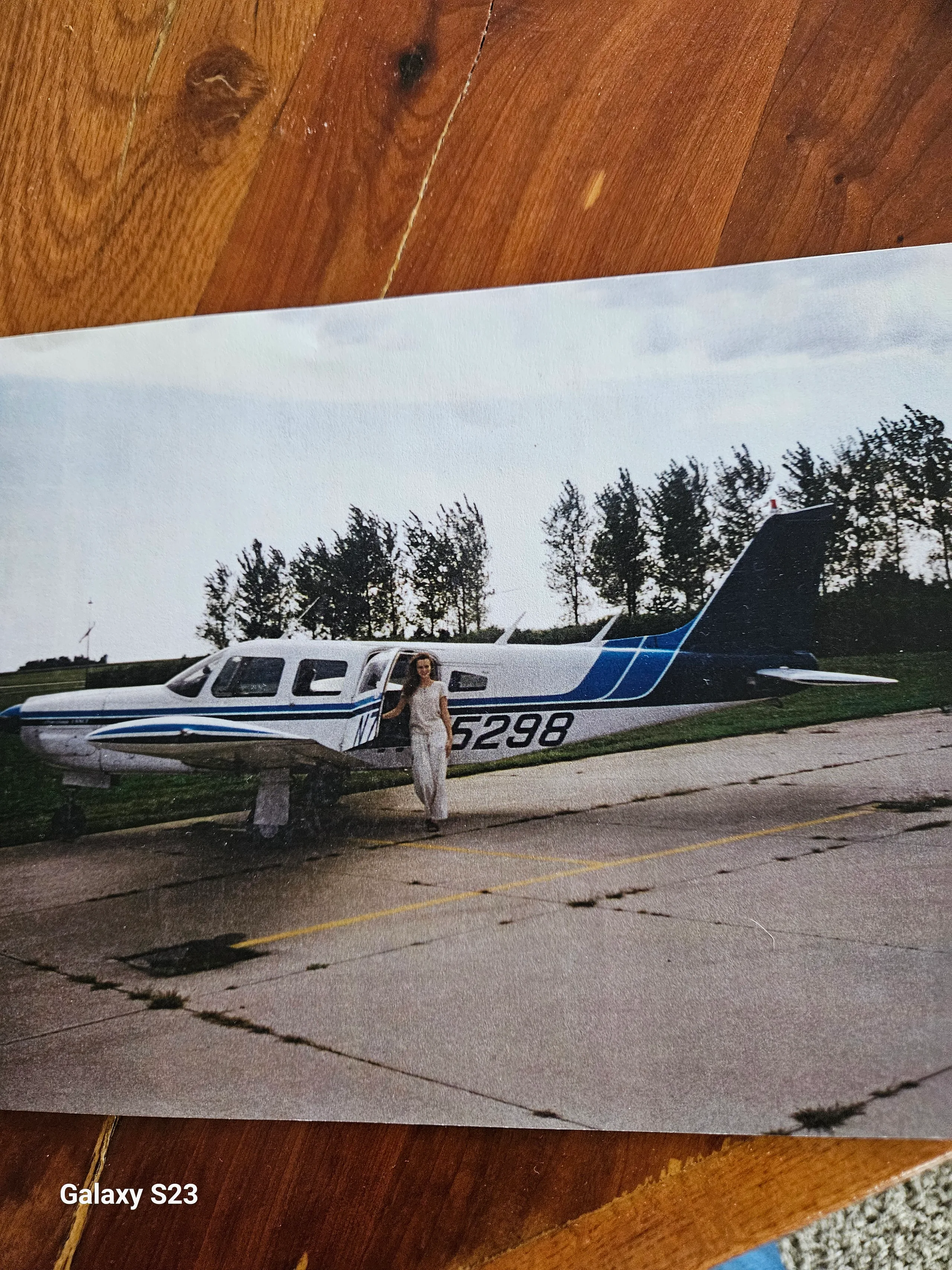 A white and blue Piper PA-32R-300 Lance (N75298) parked on an airfield, with a person standing by the open cabin door.