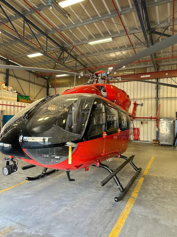 A red Airbus H145 helicopter is parked inside a hangar with its rotors extended.