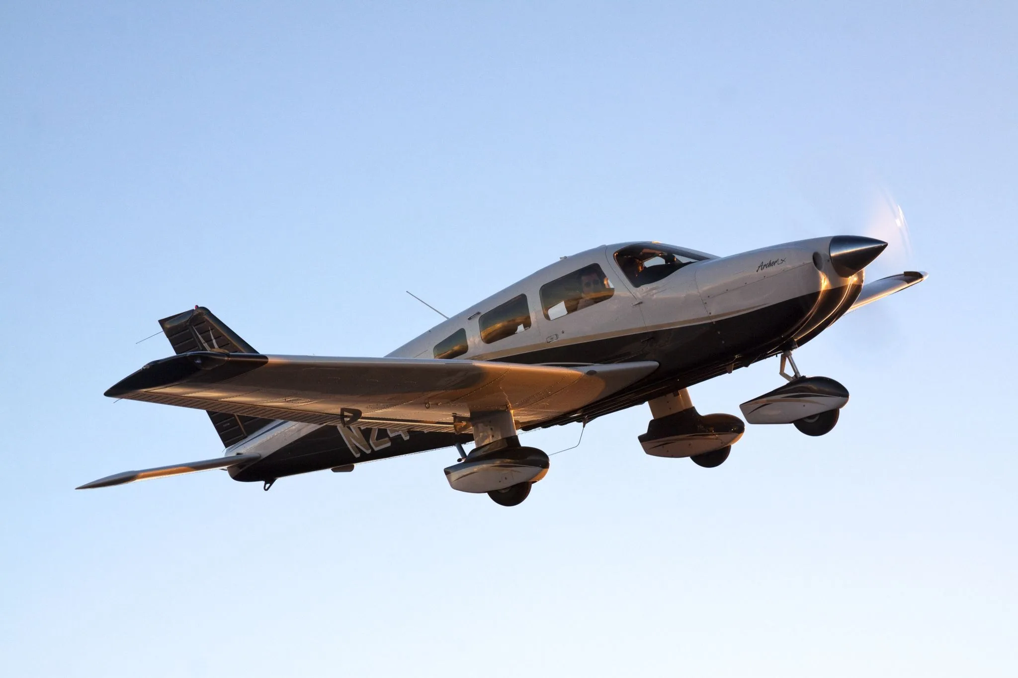 A white and black Piper Archer TX aircraft with registration N2442S is seen from below, in flight against a clear blue sky.
