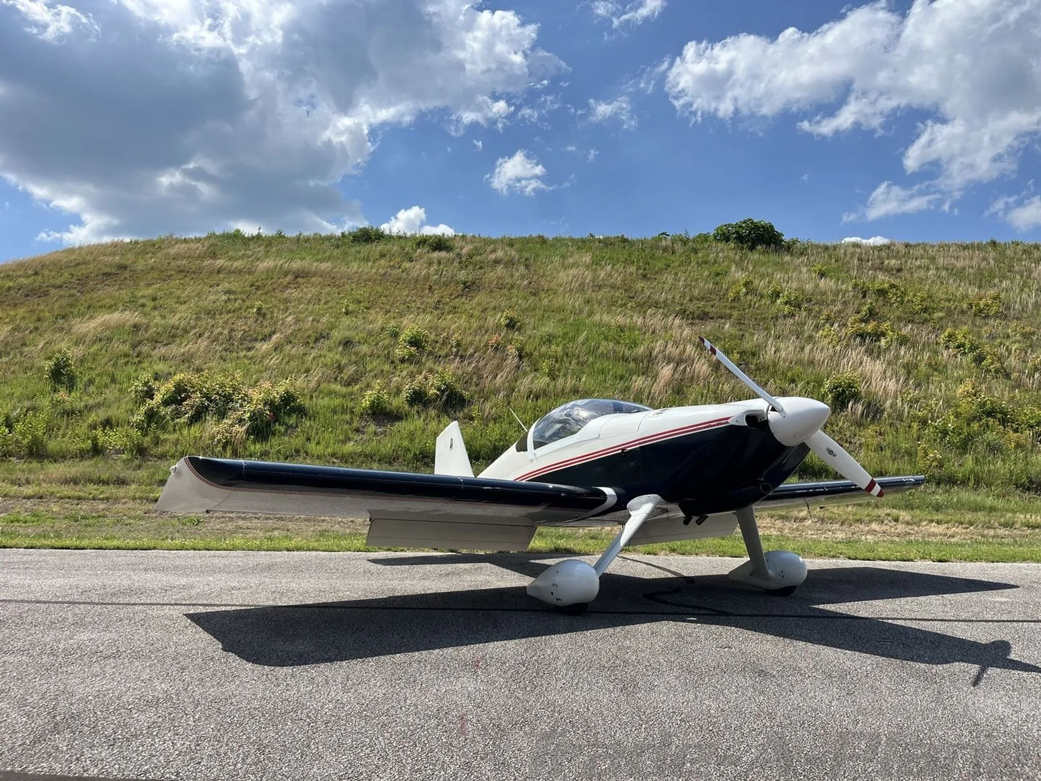 A white and dark blue single-engine aircraft with red stripes parked on an asphalt ramp, viewed from the front-right side.