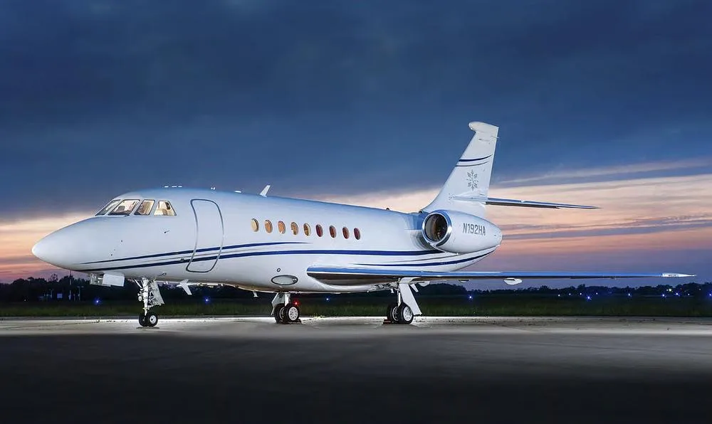 A Dassault Falcon 2000 business jet, registration N192HA, parked on an tarmac at dusk with ground lighting.