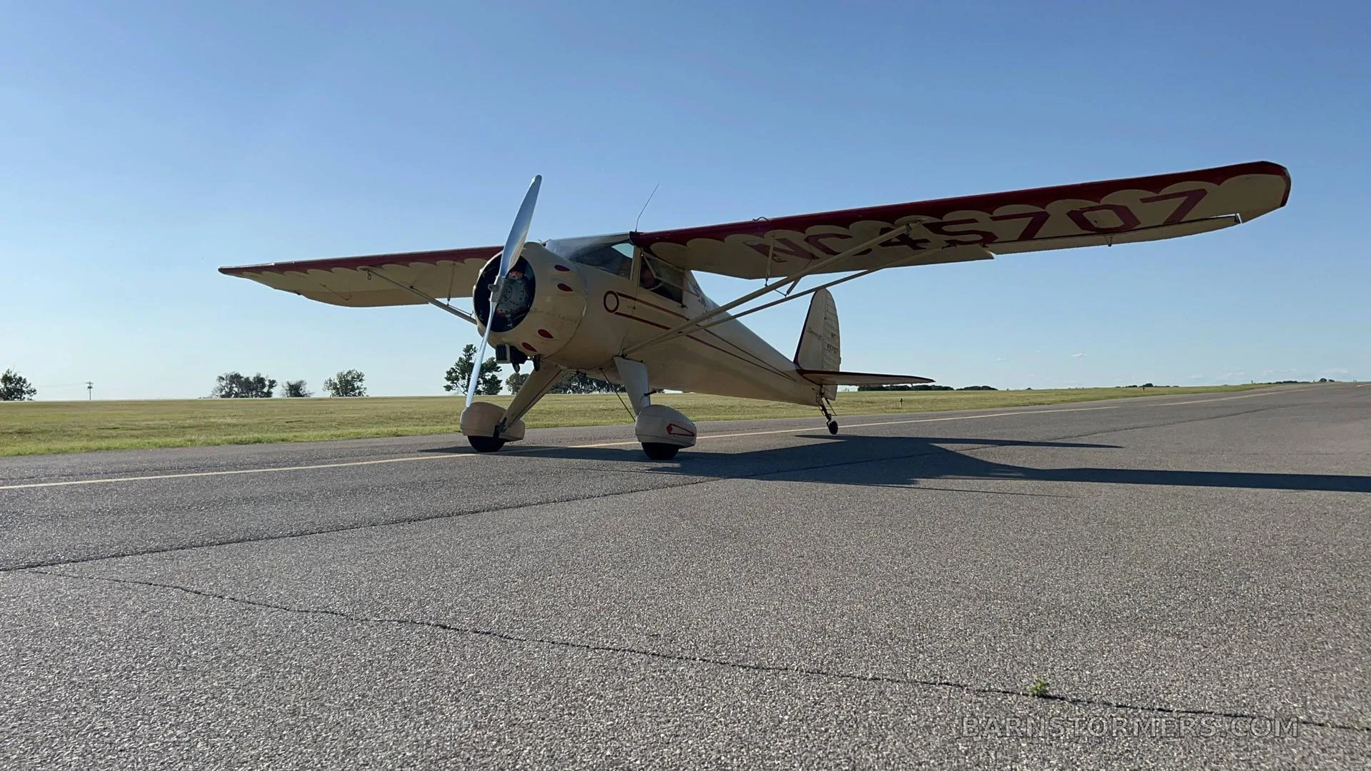 A cream-colored vintage aircraft with red trim on the wings, registration NC45707, is parked on an asphalt runway under a clear blue sky.