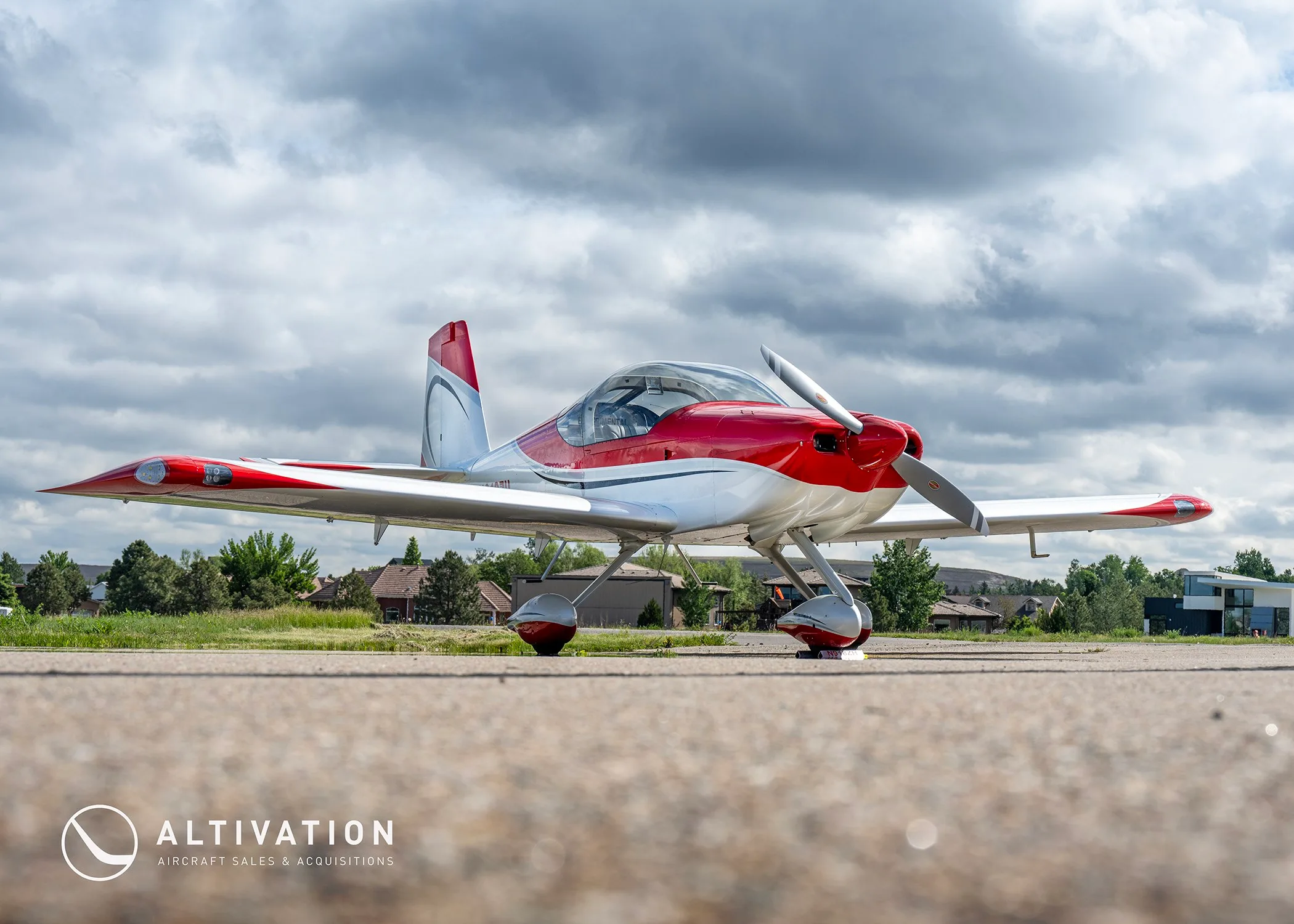A low-angle front view of the red and white N918ZH aircraft parked on an airfield under a cloudy sky.