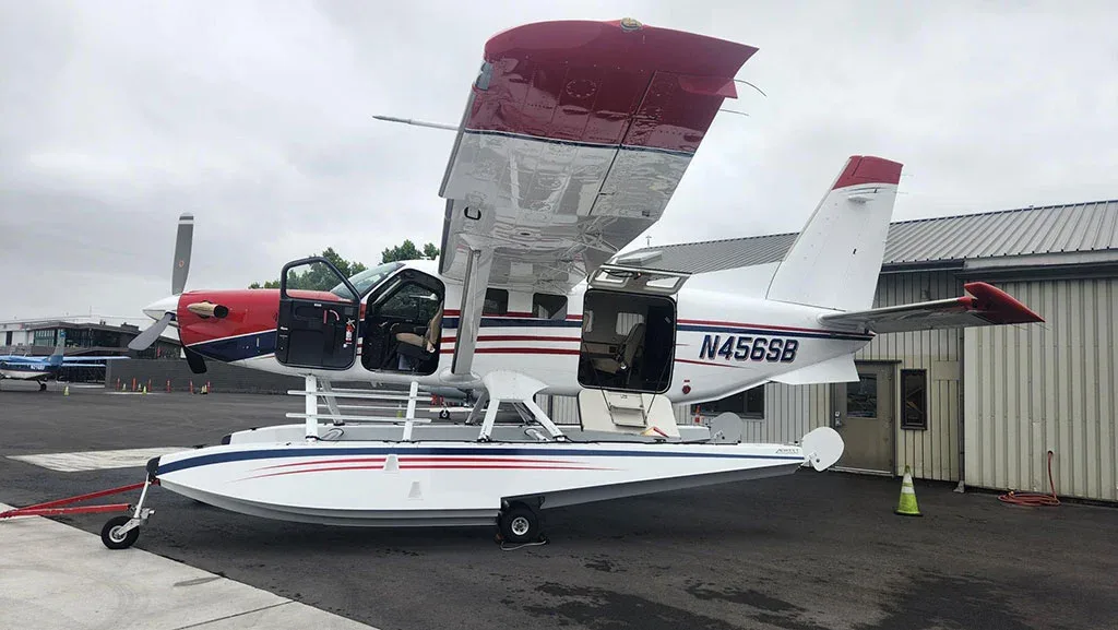 A side view of a red, white, and blue Quest Kodiak 100 on amphibious floats with its passenger and cargo doors open.