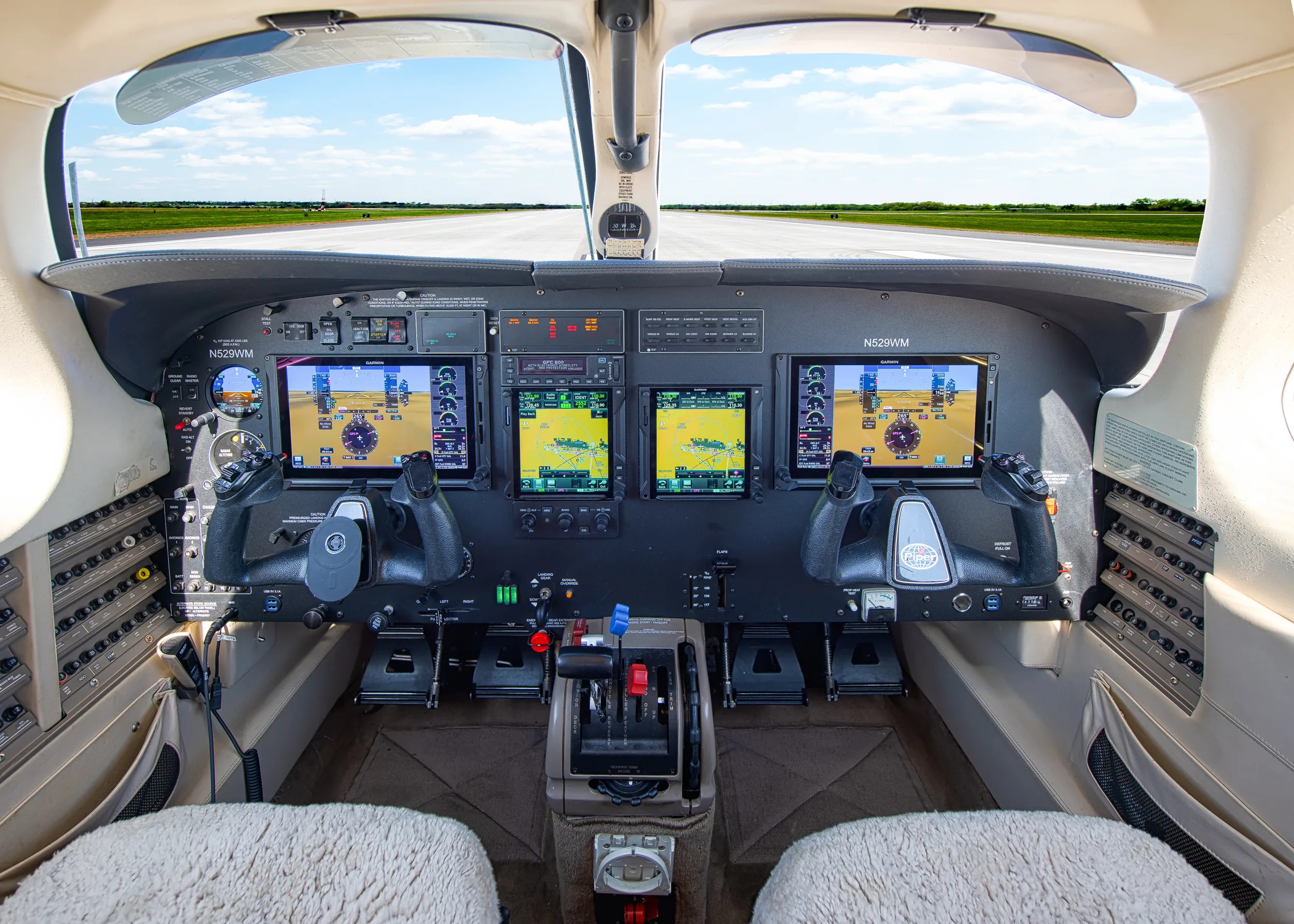 A wide view of the modern glass cockpit of the N529WM aircraft, showing multiple display screens and controls, with a runway visible through the windshield.
