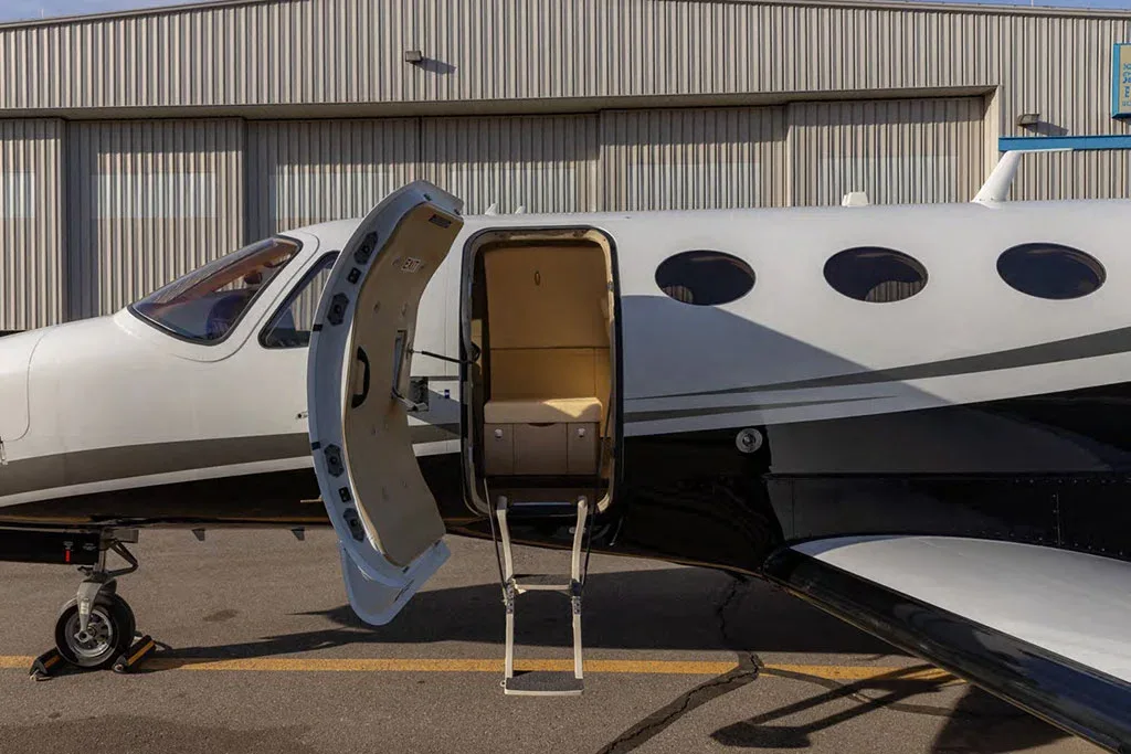 A close-up side view of a white and black private jet with its main entry door open and steps extended.