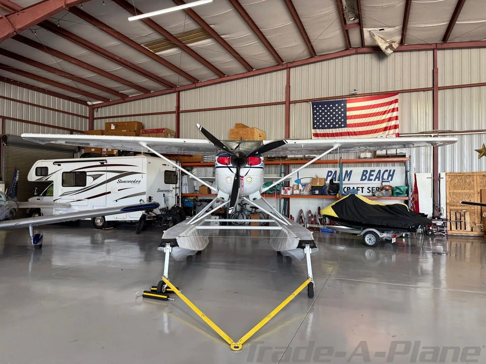 Front view of a white and blue Cessna 206 Stationair floatplane, registration N171RS, parked in a hangar.