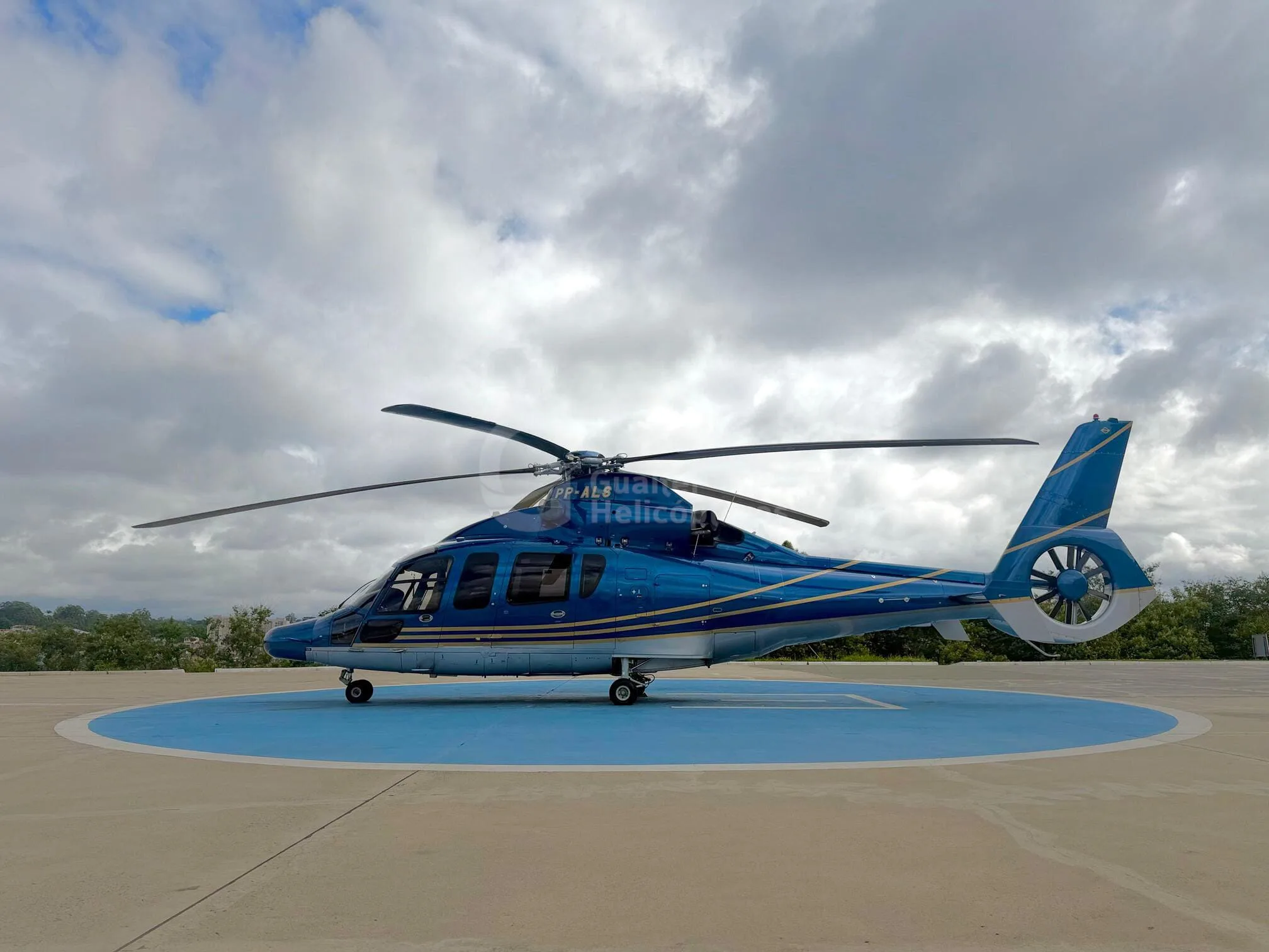 Side view of a blue and light blue helicopter with gold stripes on a helipad.
