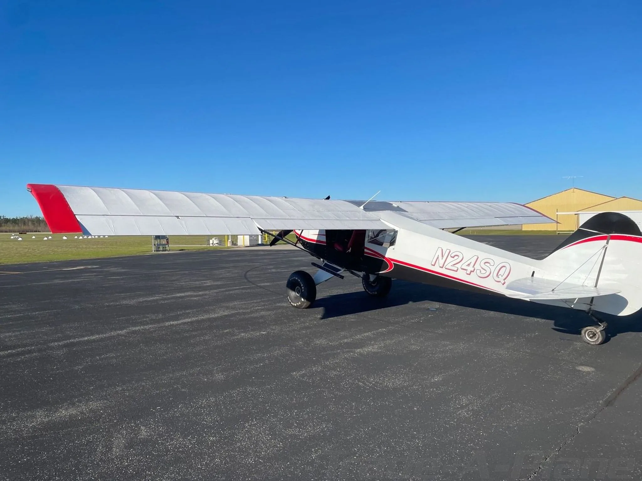 A rear-side view of the white, black, and red STOL Quest 4 aircraft (N24SQ) parked on an asphalt tarmac.